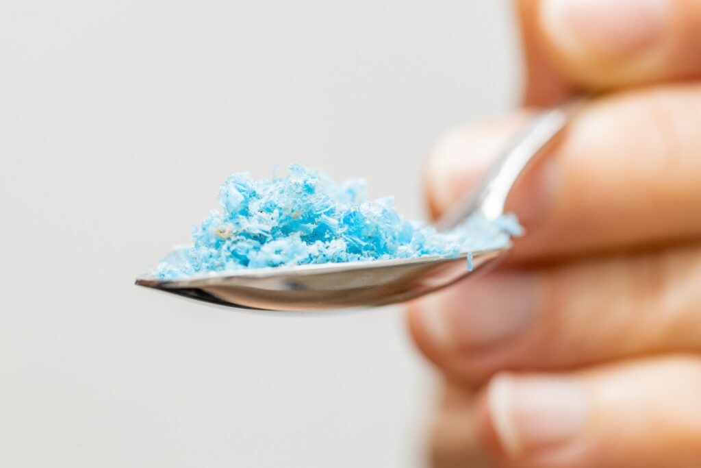 Hand holding a spoon filled with blue microplastics — plastic particles found in human blood and organs