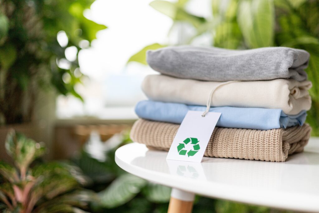 Stack of folded clothes with a recycling label tag — sustainable fabric solutions by PERMA to reduce microplastic pollution
